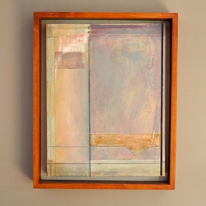 May include: Abstract painting in a wooden frame. The painting features a layered composition of muted colors, including beige, light blue, and pale pink. The colors are blended and layered to create a sense of depth and texture.