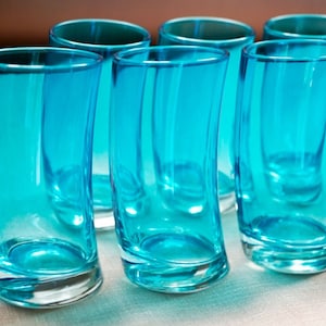 May include: Six turquoise-colored drinking glasses with a curved design. The glasses are made of transparent glass and are arranged in a group. The glasses have a modern, sleek appearance and are suitable for serving beverages.