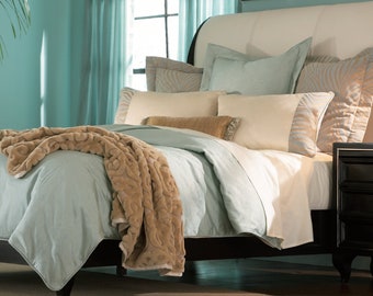 May include: A light blue bed with a brown throw blanket and white and blue patterned pillows. The bed has a headboard with a white upholstered top and a black wood frame. A black nightstand with three drawers is next to the bed.