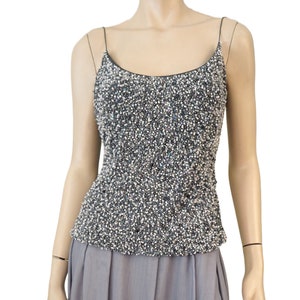 May include: A sleeveless, sequined top with a scoop neck. The top is made of a black fabric covered in small, iridescent sequins.