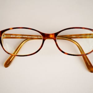 May include: Tortoise shell eyeglasses with gold metal arms and clear lenses. The brand name "JEAN LAFONT PARIS" is printed on the inside of the right lens.