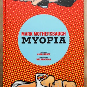以下が含まれることがあります： マーク・マザーズボーの「MYOPIA」というタイトルのハードカバー本。表紙は、ドット模様の赤い背景、タイトルが入った水色の円、イラストが特徴です。アダム・ラーナー編、ウェス・アンダーソン序文。