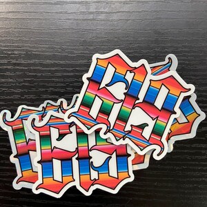 Op de afbeelding: Drie kleurrijke stickers met het woord "Hello" geschreven in een gestileerd lettertype. De stickers zijn versierd met een kleurrijk gestreept patroon dat doet denken aan een Mexicaanse serape.