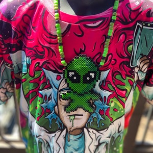 Könnte beinhalten: Eine grüne, alienförmige Perlenkette mit schwarzen Perlen. Die Kette wird von einer Person getragen, die ein buntes T-Shirt mit einer Comicfigur trägt.