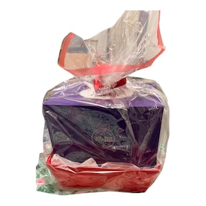Könnte beinhalten: Ein Geschenk-Korb mit roter rechteckiger Basis, der eine violette Schachtel enthält, die in transparente Zellophanfolie eingewickelt ist. Das Zellophan ist mit einem roten Band gebunden. Auf der Schachtel steht "SEED & SEAL".