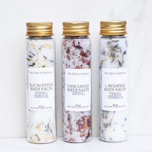 Puede incluir: Tres botellas de vidrio con tapas doradas, cada una con sales de baño. Las etiquetas dicen "Eucalyptus Bath Salts", "Unscented Bath Salts" y "Lavender Bath Salts". Las botellas están llenas de una mezcla de sales y botánicos. También se ve el texto "Not for Consumption".