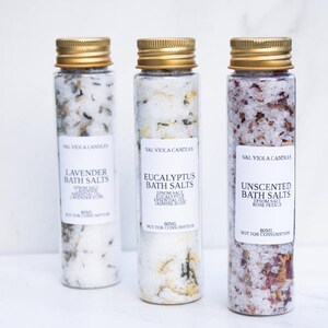 May include: Three glass bottles with gold lids, filled with bath salts. Each bottle has a white label with black text. The labels read "Lavender Bath Salts", "Eucalyptus Bath Salts", and "Unscented Bath Salts". The bottles contain 80ml of product.