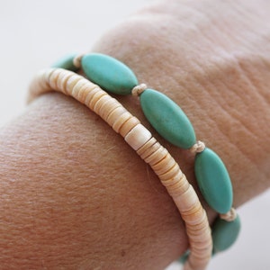 May include: A bracelet made of two strands of beads. One strand is made of small, light brown beads. The other strand is made of larger, oval-shaped turquoise beads.