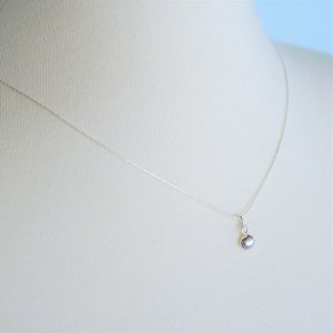 May include: A delicate silver chain necklace with a small, smooth, oval-shaped pendant.
