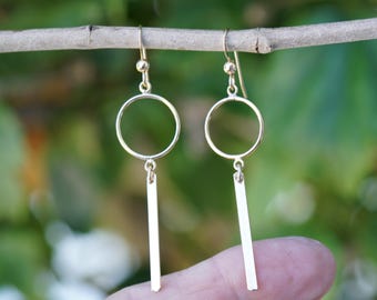 May include: Gold dangle earrings with a circle and a vertical bar pendant.