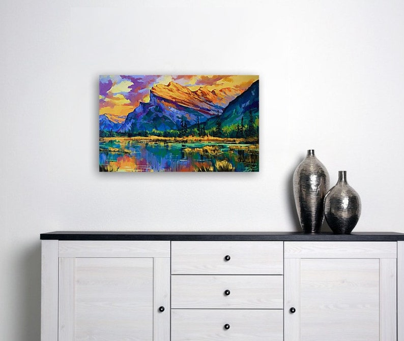 May include: A painting of a mountain range with a lake in the foreground. The mountains are a mix of blue, purple, and yellow, and the lake is a deep blue. The sky is a light blue with some clouds. The painting is done in a painterly style, with visible brushstrokes.