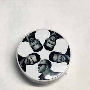 May include: A white round phone grip with a black and white image of five men's faces. The men are all looking in different directions.