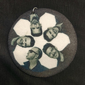 May include: A round, white, and black ornament with a snowflake design featuring five black and white images of men's faces.