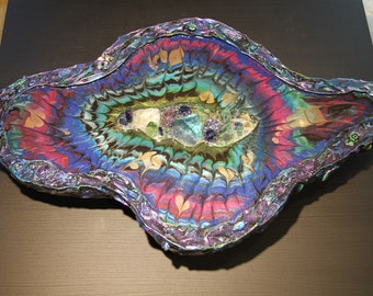 May include: A decorative, handcrafted tray with a unique, abstract design. The tray features a vibrant, multicolored pattern in shades of blue, pink, green, and gold. The edges are embellished with a textured, iridescent trim, and the center is adorned with small, colorful stones.