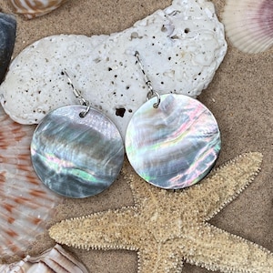May include: A pair of iridescent shell earrings with silver hooks. The earrings are round and have a pearly sheen.