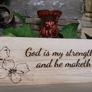 Op de afbeelding: Een houten bord met een bloemenontwerp en de tekst "God is mijn kracht en macht: en Hij maakt mijn weg volmaakt 2 Samuel 22:30".