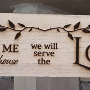 May include: A rectangular wooden sign with the text "As for me and my house we will serve the LORD" in dark brown lettering. A decorative vine is etched across the top. The sign is hung with twine.