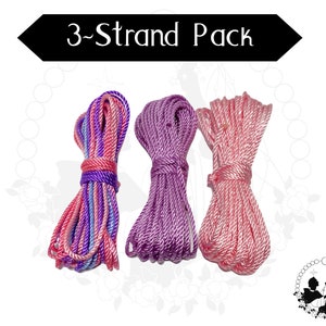 May include: Three spools of cord for making jewellery. The cords are pink and white, purple, and a mix of pink, purple, and white.