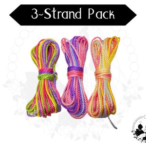 May include: Three strands of colorful embroidery floss, each with a different color combination. The strands are pink, yellow, and green; purple, white, and pink; and pink, yellow, and white.
