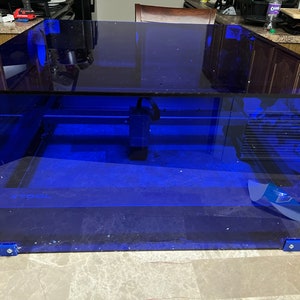 Pode incluir: Uma caixa de corte a laser de acrílico azul com uma cabeça de laser preta e um logotipo XTOOL preto na base.