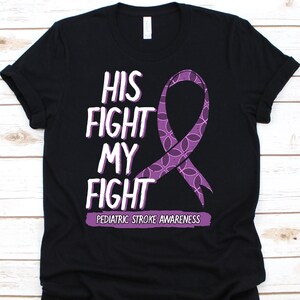 Puede incluir: Camiseta negra con el texto blanco "HIS FIGHT MY FIGHT" y un lazo morado. Debajo está "PEDIATRIC STROKE AWARENESS" en morado. La camiseta es de cuello redondo.