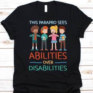 May include: Black t-shirt with the text "THIS PARAPRO SEES ABILITIES OVER DISABILITIES" and a graphic of four diverse children. The children are holding books and wearing various outfits.