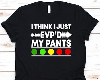 May include: Black t-shirt with white text that reads "I THINK I JUST EVP'D MY PANTS." The design includes a sound wave graphic and four colored circles: green, yellow, and red. A fun, novelty tee.