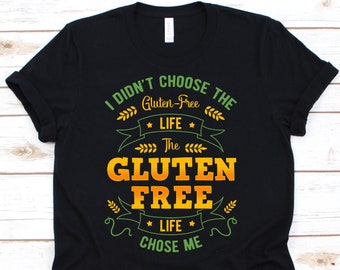 Op de afbeelding: Zwart T-shirt met de tekst "I didn't choose the Gluten-Free Life, the Gluten Free Life chose me" in groen en oranje. Het ontwerp bevat tarwe- en banerelementen.