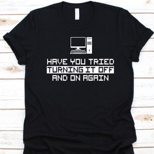 May include: Black t-shirt with a white computer graphic and the text "HAVE YOU TRIED TURNING IT OFF AND ON AGAIN". The design uses a pixelated font and computer illustration.