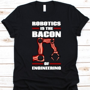 May include: Black t-shirt with the text "ROBOTICS IS THE BACON OF ENGINEERING" in white. The design includes a robotic arm made to look like bacon. The shirt is a crew neck.
