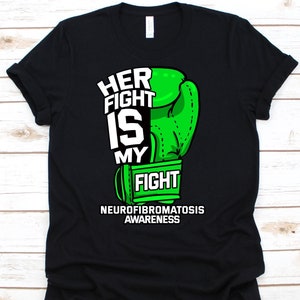 Könnte beinhalten: Schwarzes T-Shirt mit einem grünen Boxhandschuh-Motiv. Der Text "HER FIGHT IS MY FIGHT" ist weiß, darunter steht "NEUROFIBROMATOSIS AWARENESS". Das Design ist mittig auf dem Shirt platziert.