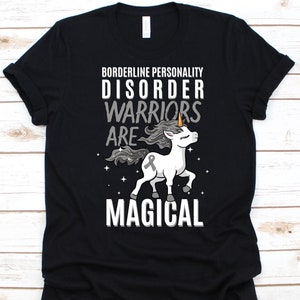 May include: Black t-shirt featuring the text "Borderline Personality Disorder Warriors Are Magical" and a white unicorn graphic. The unicorn has a grey ribbon and is set against a starry background.