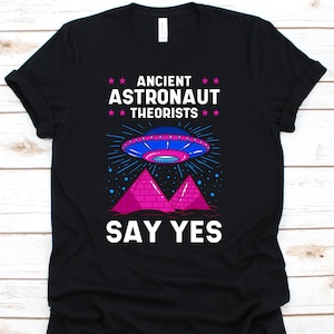 May include: Black t-shirt with a graphic featuring a blue and pink UFO above pink pyramids. The text reads "ANCIENT ASTRONAUT THEORISTS SAY YES" in white and pink.