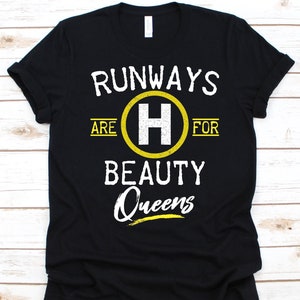May include: Black t-shirt with the text "RUNWAYS ARE FOR BEAUTY QUEENS" in white and yellow. The letter "H" is inside a yellow circle. The shirt is a crew neck.