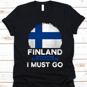 Może przedstawiać: Czarny t-shirt z postarzaną grafiką fińskiej flagi w białym okręgu. Poniżej flagi tekst: "FINLAND IS CALLING I MUST GO" w kolorze białym i niebieskim.