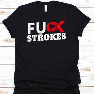 Puede incluir: Camiseta negra con la frase "F*CK STROKES" en fuente blanca desgastada y un lazo rojo. La camiseta es de material suave y tiene un cuello redondo clásico.