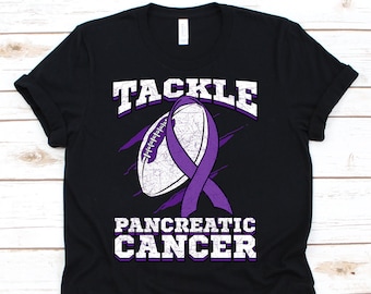 May include: Black t-shirt with a distressed graphic. The design features a football, a purple awareness ribbon, and the words "TACKLE PANCREATIC CANCER" in white and purple lettering. The shirt is made of a soft material.