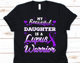 May include: Black t-shirt with the text "My Beautiful Daughter is a Lupus Warrior" in white and purple. The design includes purple hearts and a purple awareness ribbon. A casual tee for awareness.