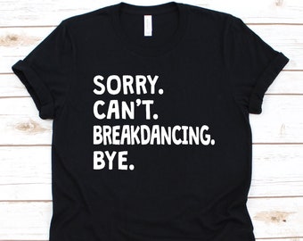 Puede incluir: Camiseta negra con el texto blanco "SORRY. CAN'T. BREAKDANCING. BYE." La camiseta está hecha de un material suave y tiene un diseño clásico de cuello redondo. El texto está centrado en la parte delantera de la camiseta.