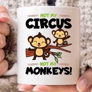 Puede incluir: Taza de cerámica blanca con el texto "NOT MY CIRCUS NOT MY MONKEYS!" e ilustraciones de dos monos de dibujos animados en una rama. Los monos son marrones con caras color canela y están sonriendo. El texto es en negro y verde.