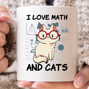 May include: White ceramic mug with the text "I LOVE MATH AND CATS". The mug features a cartoon cat wearing red glasses, with math symbols and graphs in the background. The mug is held by a person.