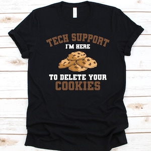May include: Black t-shirt with the text "TECH SUPPORT I'M HERE TO DELETE YOUR COOKIES" in brown and white. The design includes an illustration of chocolate chip cookies. A humorous tech-themed graphic tee.