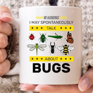 May include: White ceramic mug with a handle, featuring colorful illustrations of various insects and the text "WARNING I MAY SPONTANEOUSLY TALK ABOUT BUGS". The mug has a glossy finish and is held by a person.