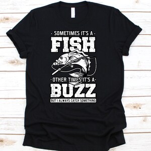 May include: Black t-shirt with a white graphic featuring a fish and the word "FISH" above it. The text reads "Sometimes it's a fish, other times it's a buzz, but I always catch something."