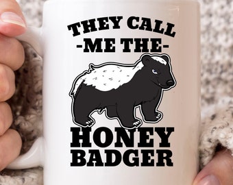 May include: White ceramic mug featuring a black and white illustration of a honey badger with the text "THEY CALL -ME THE- HONEY BADGER" in bold black letters. The mug has a white handle.