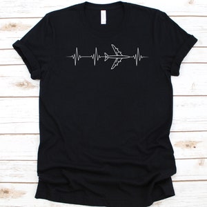 以下が含まれることがあります： 飛行機の白いグラフィックが心拍ラインに組み込まれた黒いTシャツ。このデザインは、航空に関連するテーマを示唆しています。このシャツは柔らかい素材で作られています。