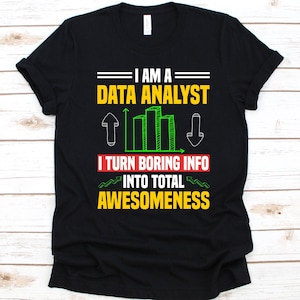 Może przedstawiać: Czarna koszulka z napisem "I AM A DATA ANALYST I TURN BORING INFO INTO TOTAL AWESOMENESS" w kolorze żółtym, białym i zielonym. Projekt zawiera wykres słupkowy i strzałki.