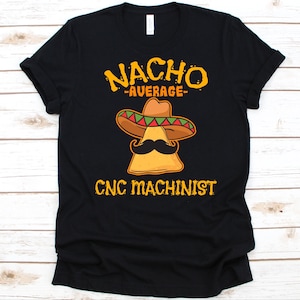 May include: Black t-shirt with a graphic featuring a nacho chip wearing a sombrero and mustache. The text reads "NACHO AVERAGE CNC MACHINIST" in yellow and orange. The design is centered on the front of the shirt.