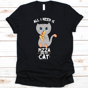 May include: Black t-shirt featuring a gray cartoon cat eating pizza. The text "ALL I NEED IS PIZZA AND MY CAT" is above and below the cat illustration. The shirt is made of a soft material.