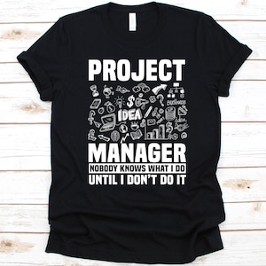 Puede incluir: Camiseta negra con texto blanco y garabatos. La camiseta dice "PROJECT MANAGER" encima de "NOBODY KNOWS WHAT I DO UNTIL I DON'T DO IT". El diseño incluye iconos relacionados con los negocios y las ideas.